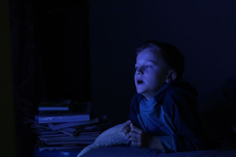 Child watching TV in dark room, illuminated by screen, home entertainment, nighttime activity.