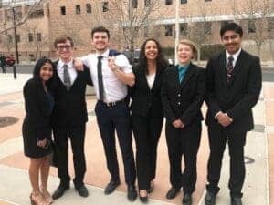 Diverse students in formal attire smiling outside Albuquerque Academy campus.