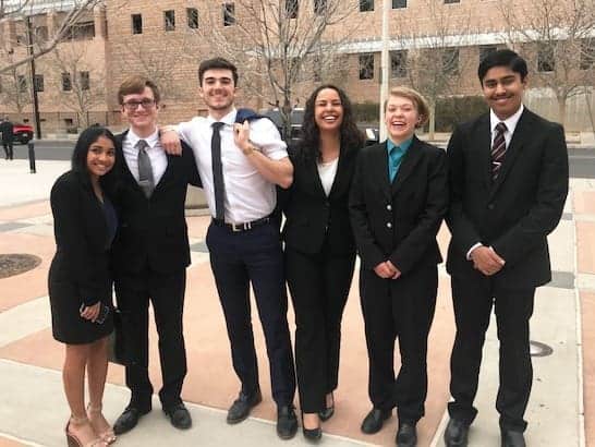 Diverse students in formal attire smiling outside Albuquerque Academy campus.