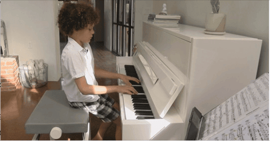 Young student playing white upright piano at Albuquerque Academy campus, music education.