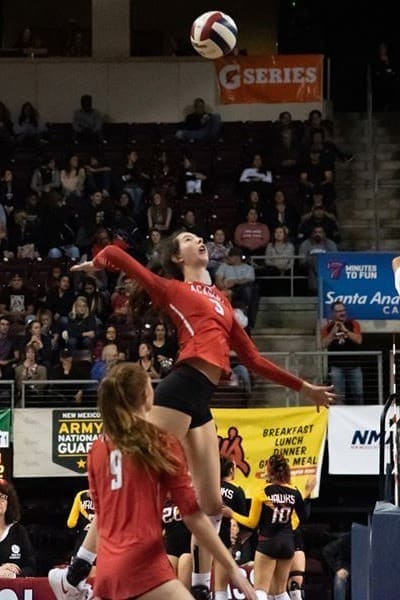 Female volleyball player jumping for ball at Albuquerque Academy gymnasium during match.