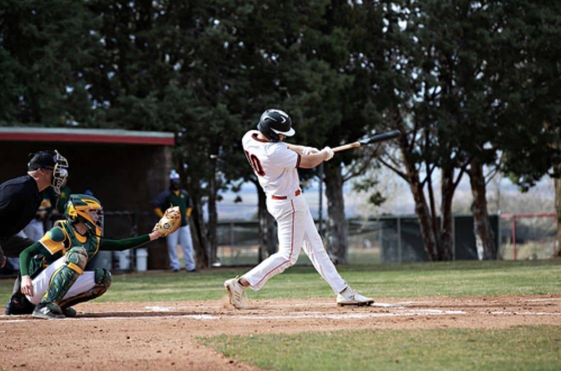 High school baseball player swinging at bat at Albuquerque Academy athletic field.