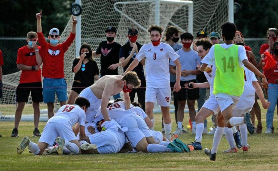 Energetic Albuquerque Academy soccer team celebrating goal on field with joyful fans and players.
