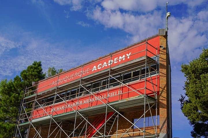 Albuquerque Academy signage on school building under blue sky and scaffolding.