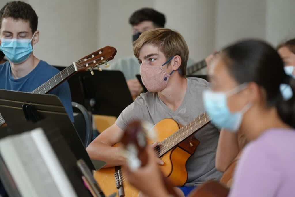 Students wearing masks playing acoustic guitars in a classroom setting.