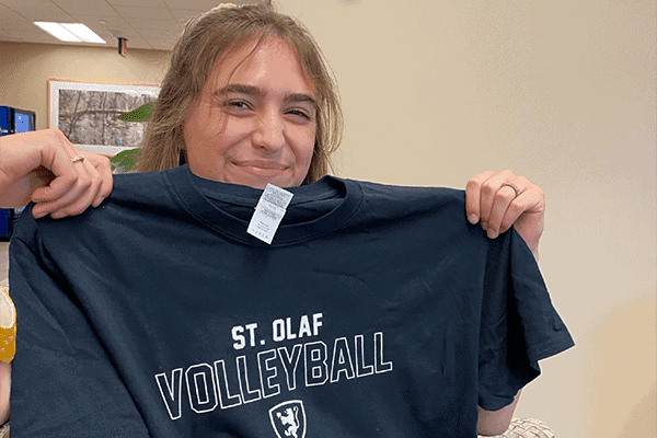 Albuquerque Academy student holding a volleyball t-shirt in school setting.