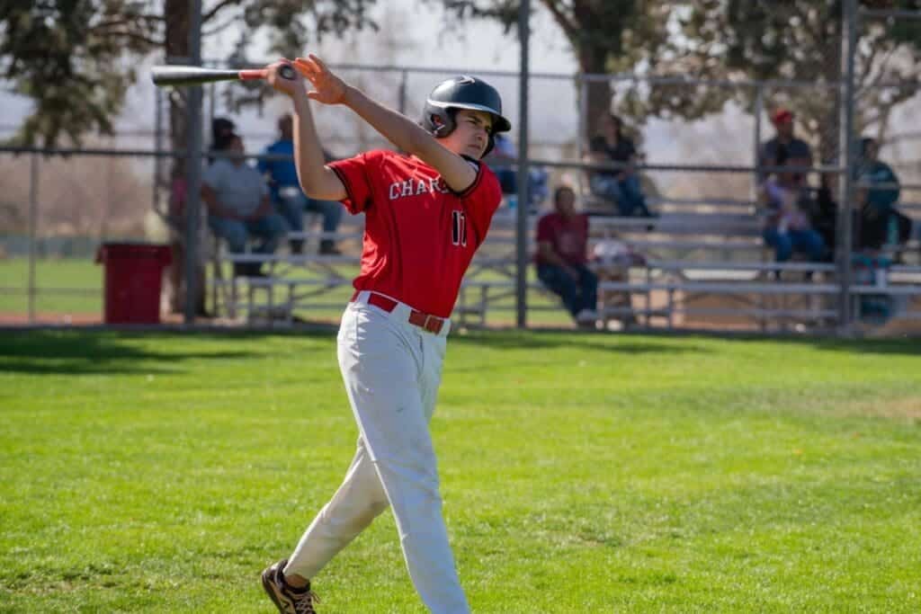 YOUNG BOY IN RED BASEBALL UNIFORM SWINGS BAT ON FIELD.