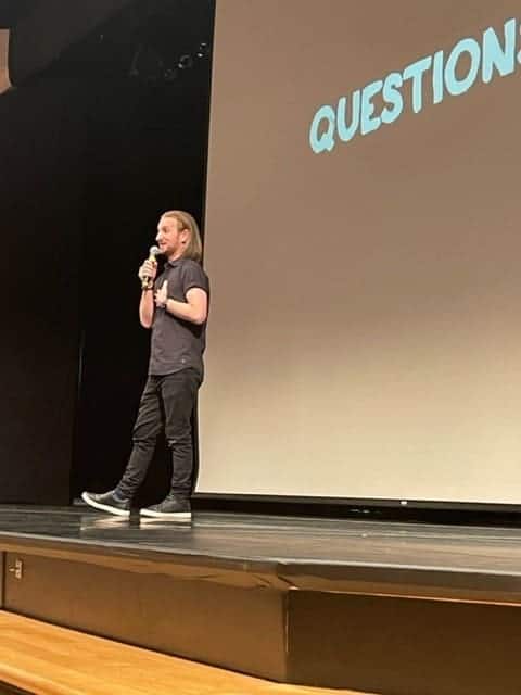 Engaged student speaking at Albuquerque Academy presentation on a stage with Question prompt on screen.