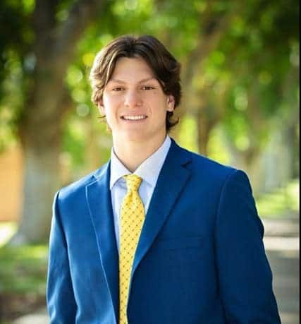 Young male student in blue blazer smiling outdoors at Albuquerque Academy campus.