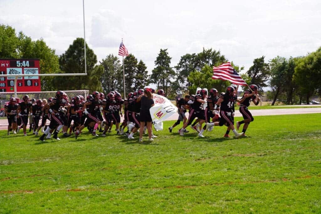 High school football team running onto the field at Albuquerque Academy.