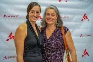 Smiling woman and older woman at Albuquerque Academy event with branded backdrop.