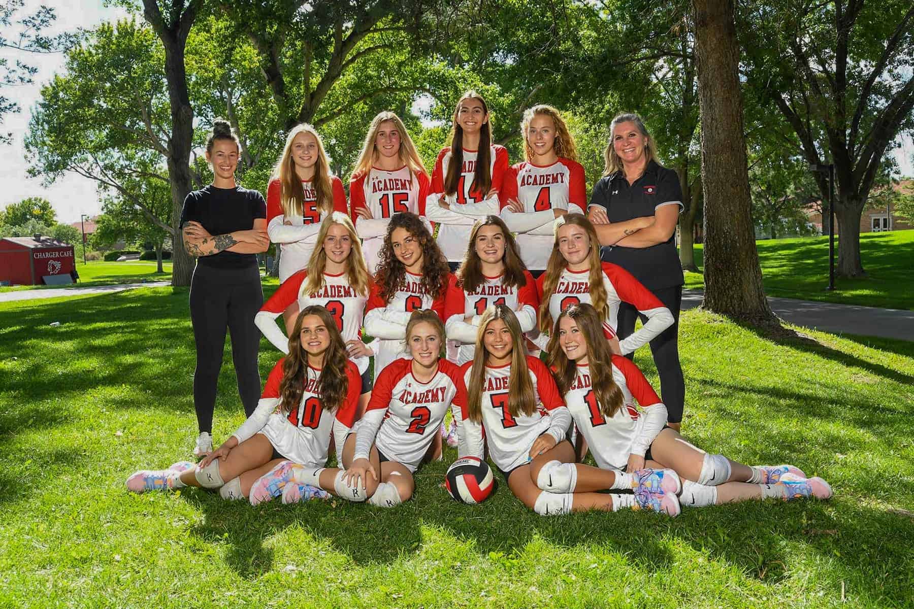 Albuquerque Academy girls volleyball team posing outdoors with coach, in red and white uniforms.