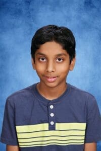 Bright young student at Albuquerque Academy with a blue background and casual attire.