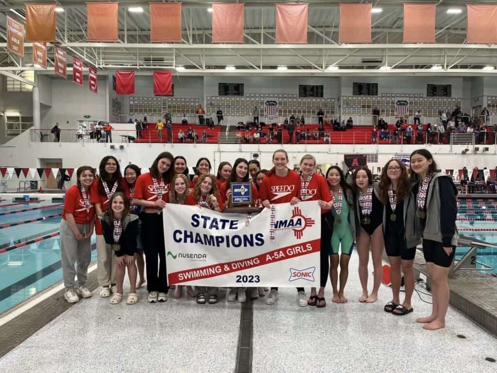 Young female swimmers celebrating age group state champions at Albuquerque Academy indoor swimming pool.