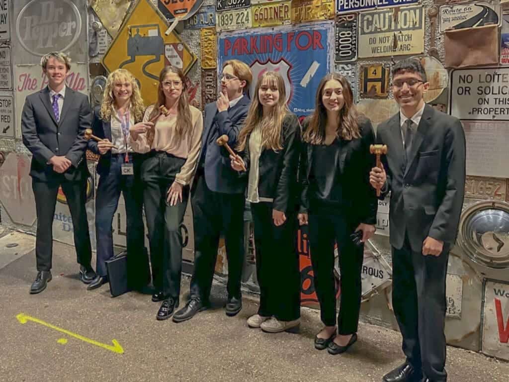 Intelligent students in business attire holding gavel props at Albuquerque Academy event.