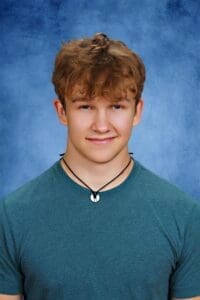 Bright male student at Albuquerque Academy with curly hair and blue background.
