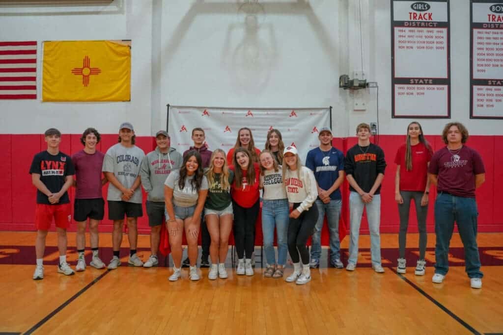 Albuquerque Academy student athletes celebrating in gymnasium with college gear on.