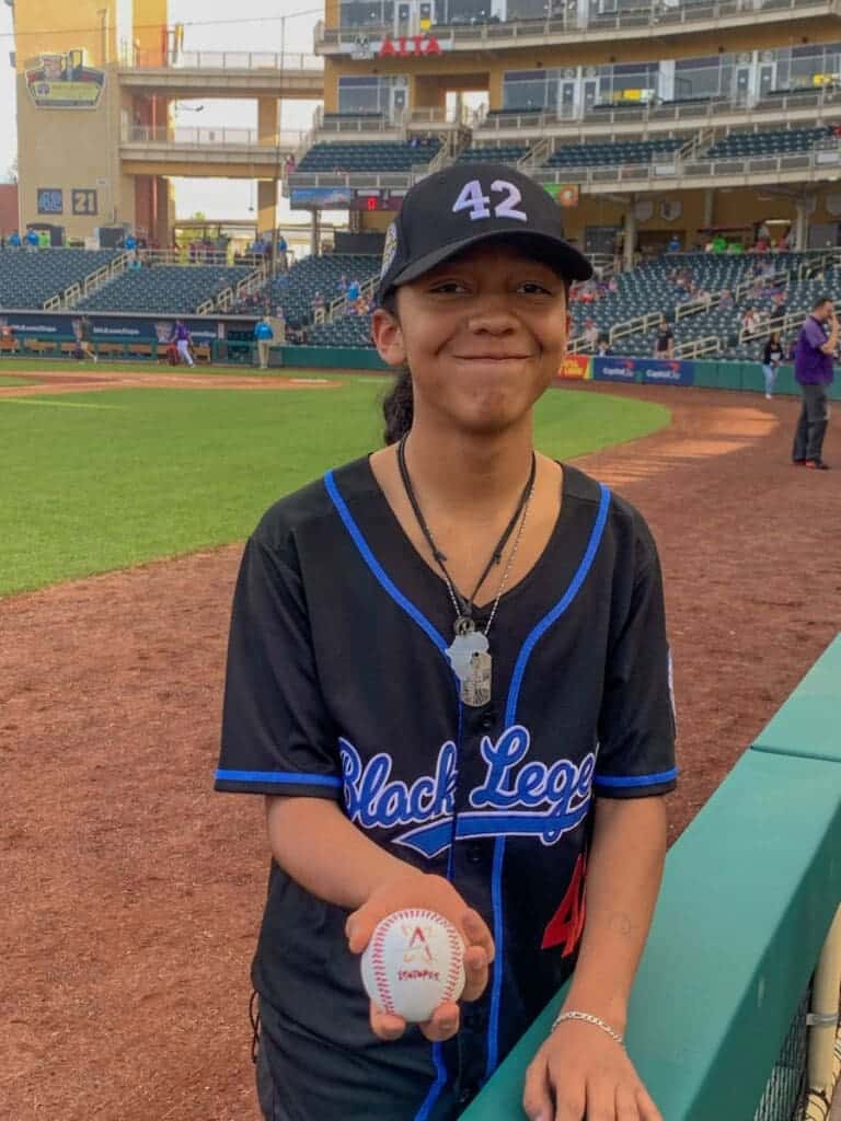 Young baseball player at Albuquerque Academy baseball game, holding a ball, smiling.