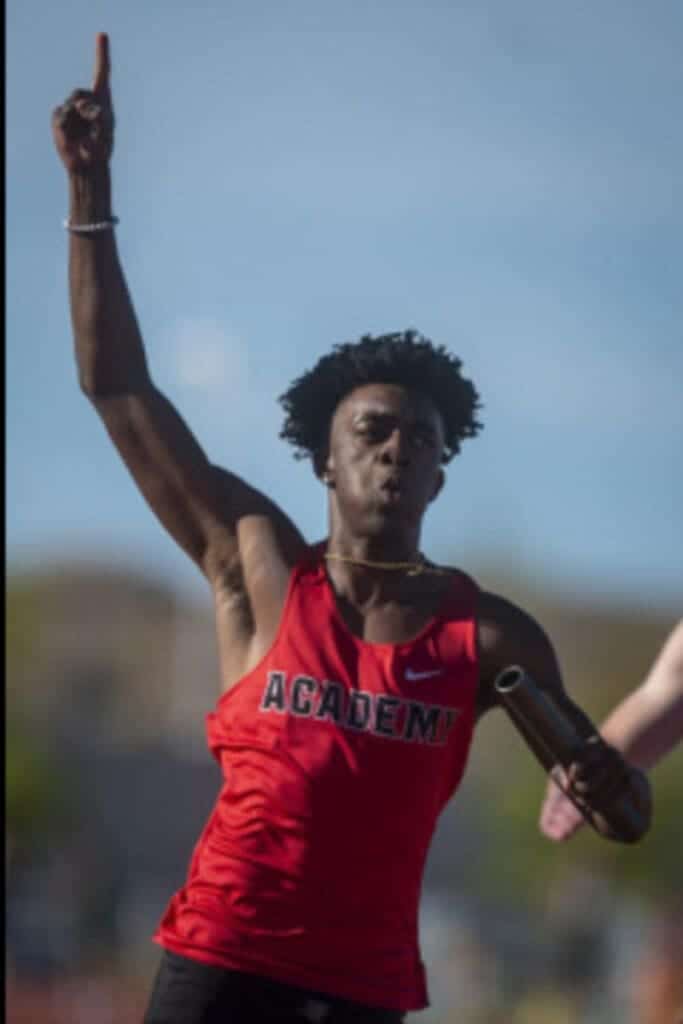 High school track athlete wearing Albuquerque Academy uniform competing outdoors.