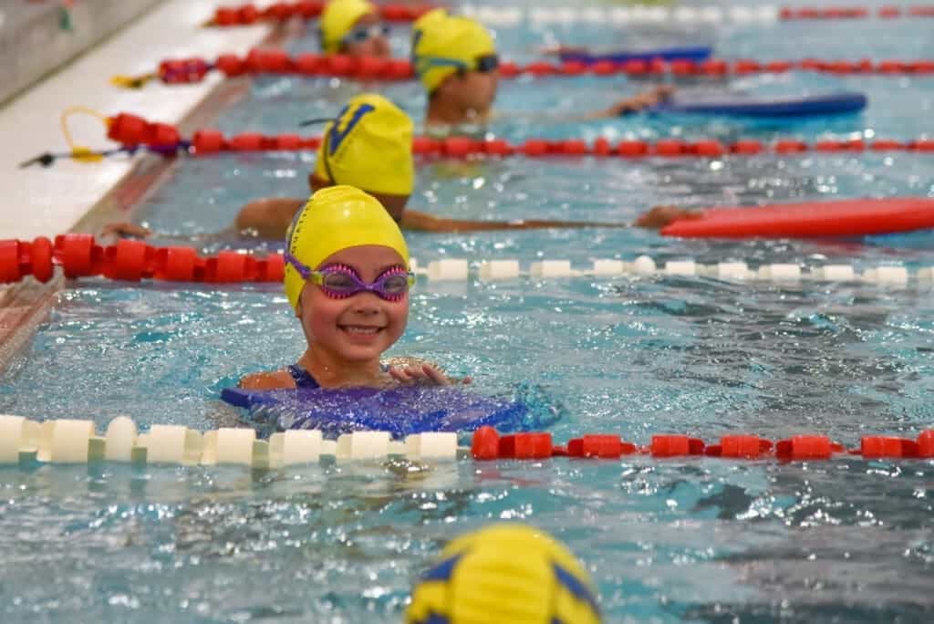 Children swimming in a competitive swimming pool wearing yellow caps and goggles.