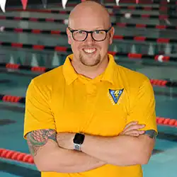 Modern male swimming coach at Albuquerque Academy swimming pool in yellow polo shirt.