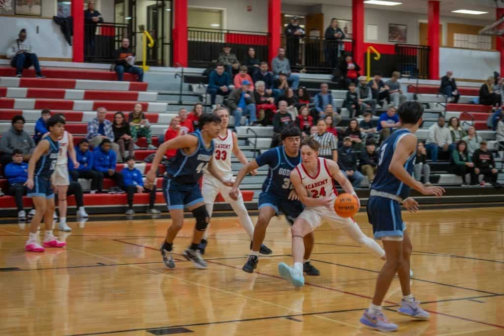 Basketball players in action during a game at Albuquerque Academy gymnasium with spectators watching.