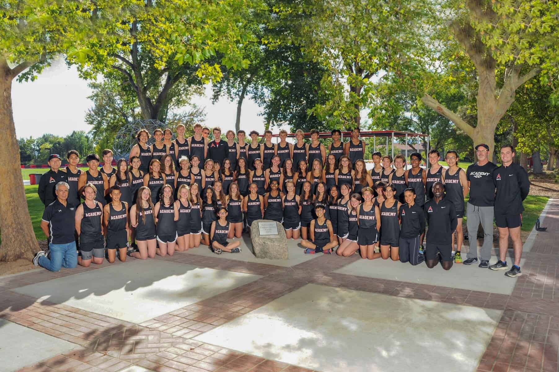Diverse Albuquerque Academy rowing team poses under large trees in athletic uniforms on campus.