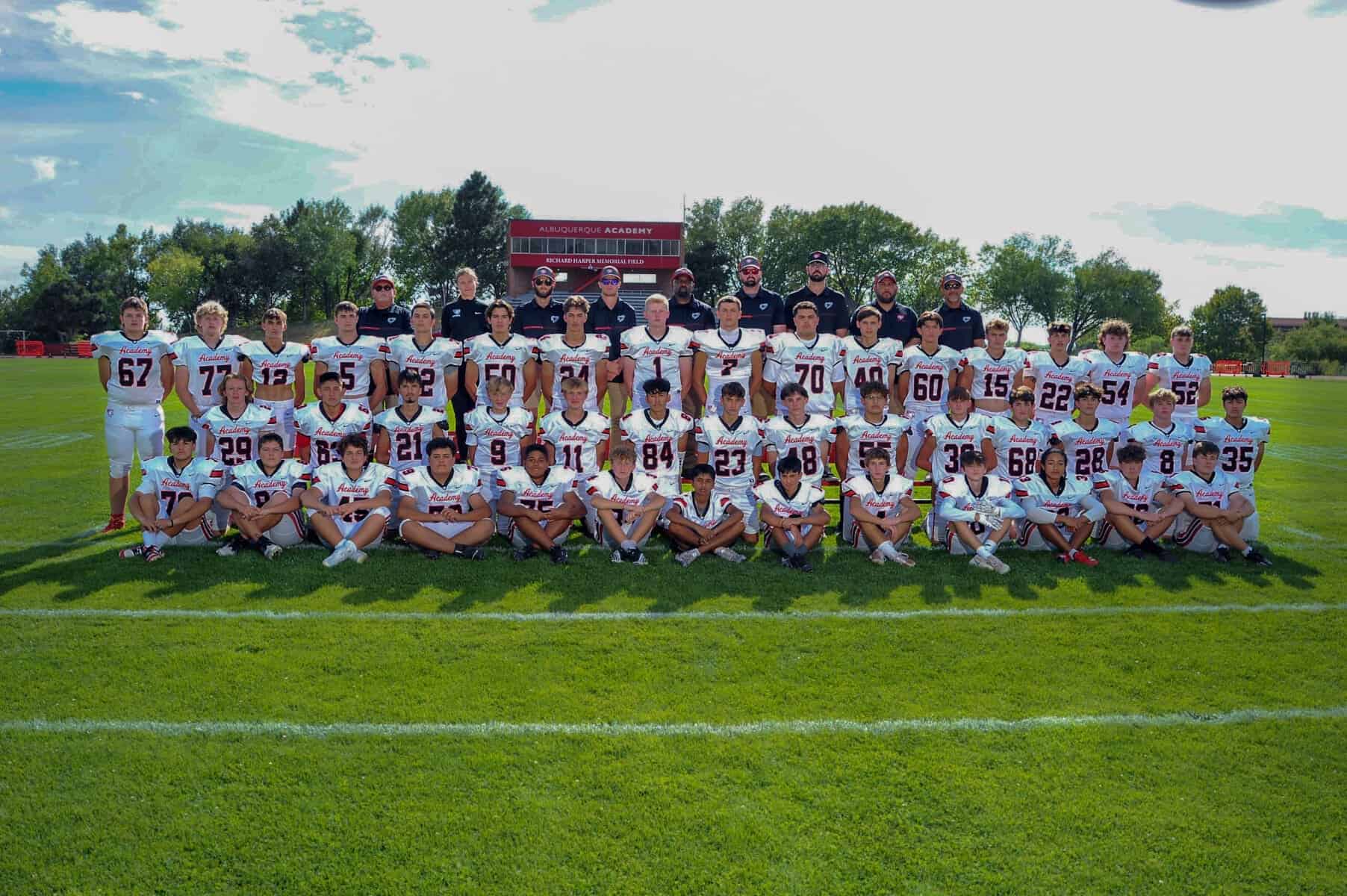 High school football team in white jerseys on grass field at Albuquerque Academy.