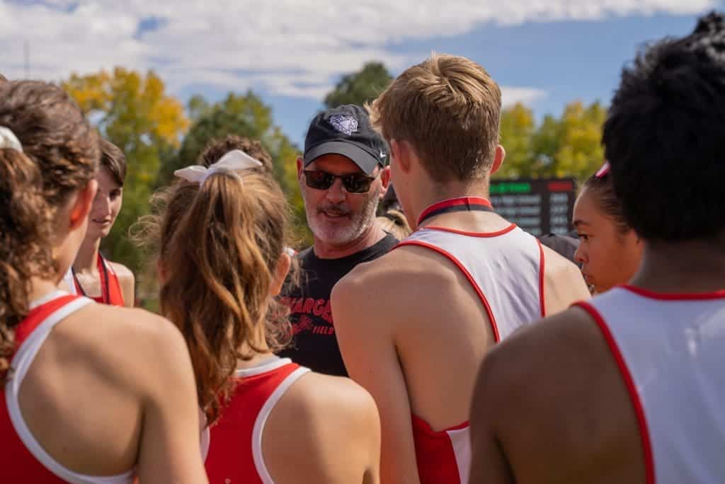 Athletic team huddle with coach providing instructions at Albuquerque Academy cross country event.