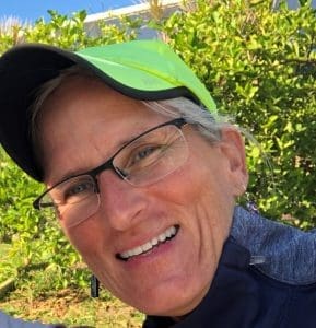 Smiling person with cap and glasses outdoors.