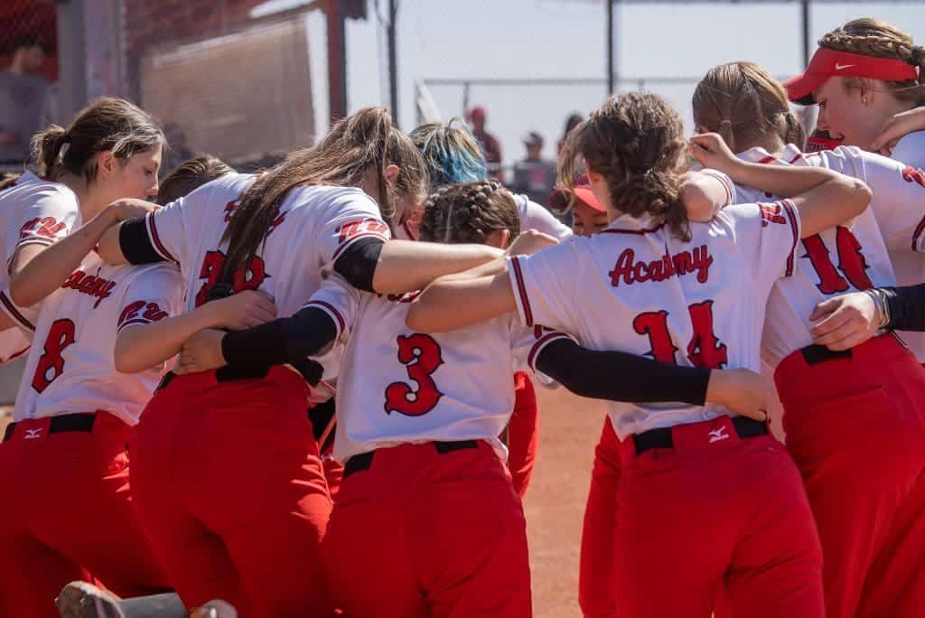 Girls softball team huddling at Albuquerque Academy sports field, showing teamwork and school spirit.