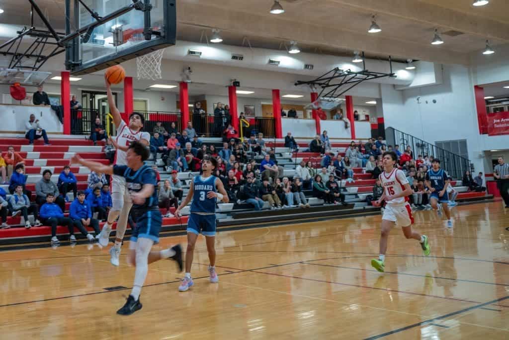Young students playing basketball during game at Albuquerque Academy gymnasium.