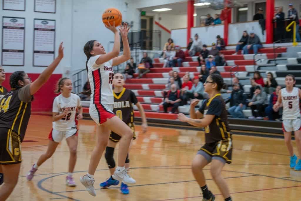Girl shooting basketball during game at Albuquerque Academy sports facility.