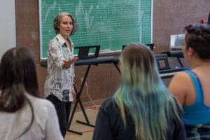 Woman teaching music class with students and keyboard.