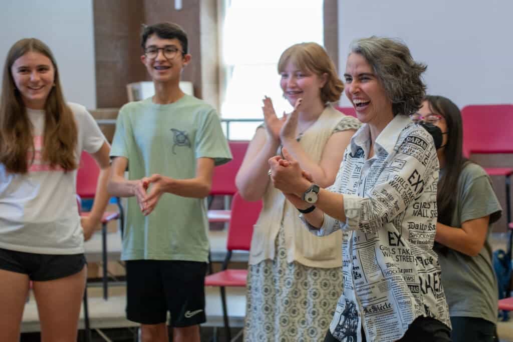 Group of students clapping with teacher in classroom.