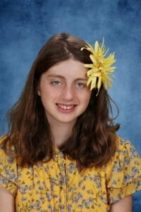 Smiling girl with yellow flower hair accessory.