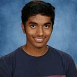 Young man smiling in color-blocked shirt, blue background.
