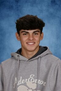 Teen boy smiling in gray hoodie against blue background.