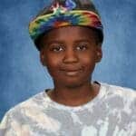 Young student wearing tie-dye shirt and colorful cap smiles confidently.