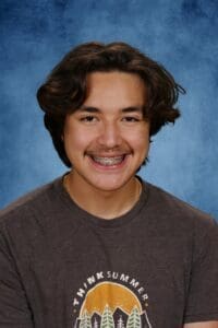 Smiling teen with braces, summer-themed shirt, blue background.