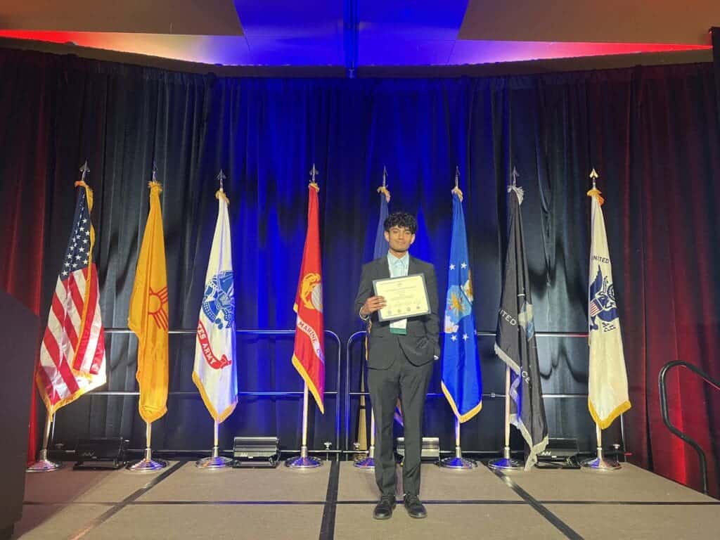 1. Student receiving award at Albuquerque Academy graduation ceremony with flags in background.