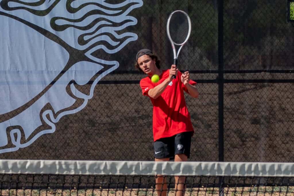 Young male tennis player hitting a rally on an outdoor court at Albuquerque Academy school.