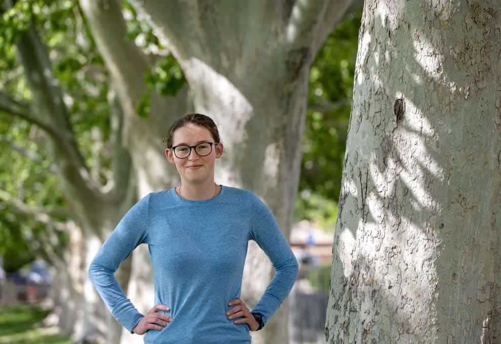 Youthful woman standing outdoors near large trees at Albuquerque Academy campus, showcasing educational environment and natural scenery.