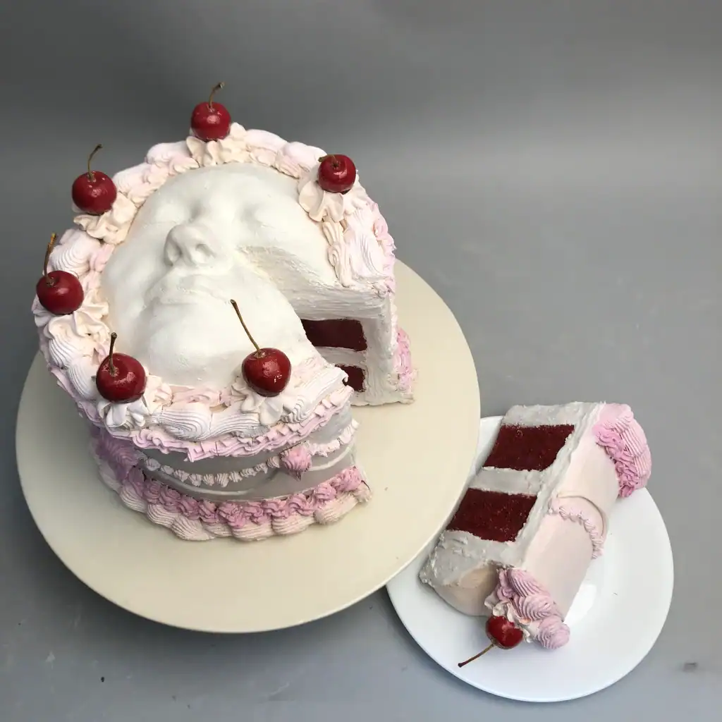 Cherry-topped face cake with pink frosting and layered sponge cake slices.