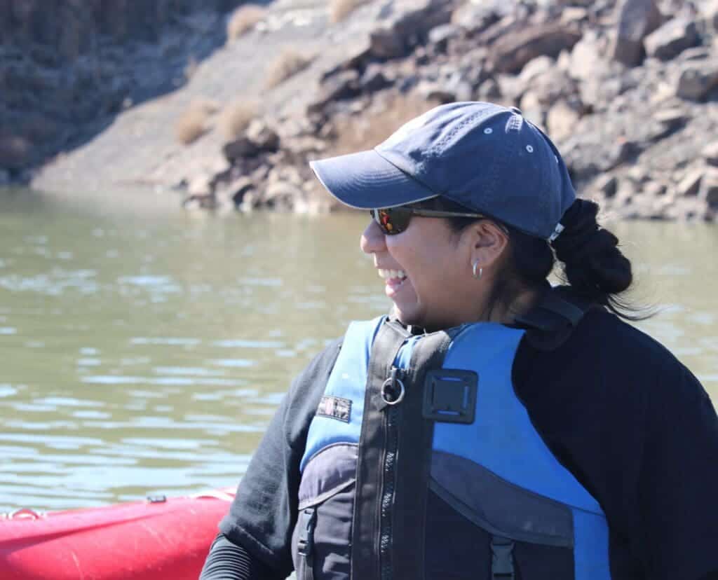 Adventurous student kayaking on a scenic river with rocky cliffs in the background.