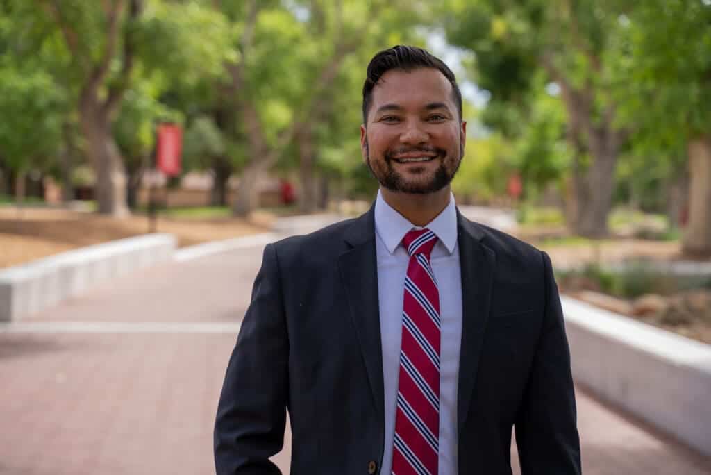 Professional man smiling outdoors on Albuquerque Academy campus with trees in background.