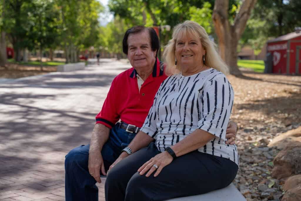 Friendly older couple sitting on a park bench amidst Albuquerque Academy campus greenery.