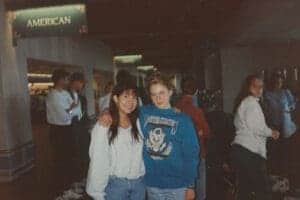 Female student and woman at Albuquerque Academy airport terminal, traveling, smiling, casual wear, diverse group, educational environment, American Airlines signage, airport scene, late 20th century imagery, airport check-in area, High School students.