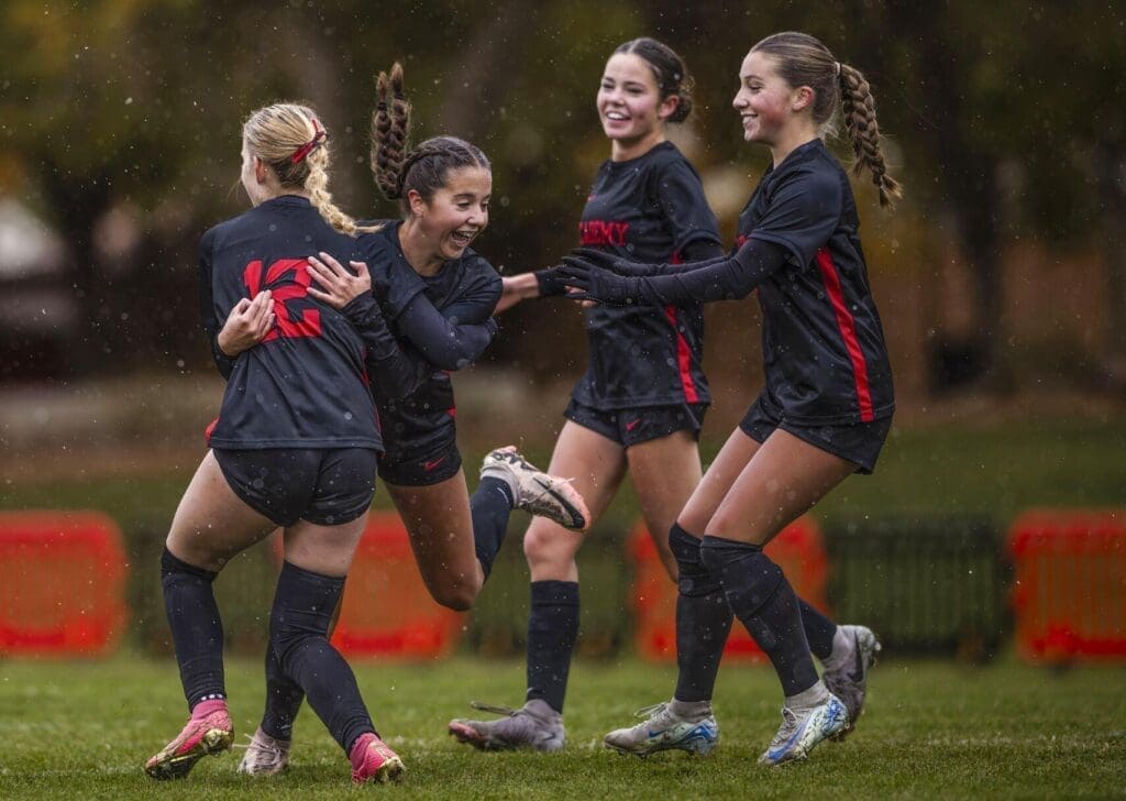 Albuquerque Academy girls soccer team celebrating outdoors in rain, showing school sports spirit and team camaraderie.