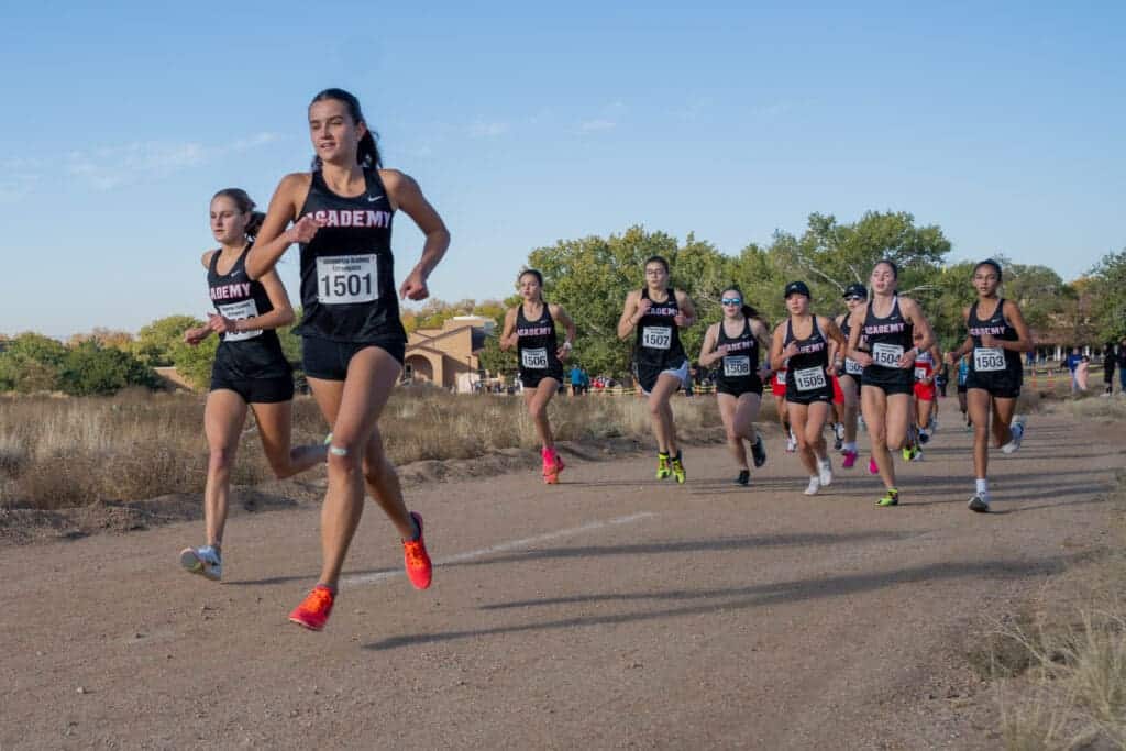 Running team of Albuquerque Academy cross country race on a dirt trail in a scenic outdoor setting.